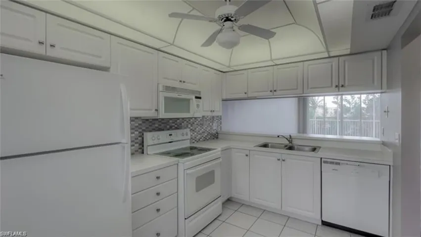 Kitchen with ceiling fan, sink, light tile patterned floors, white appliances, and white cabinets