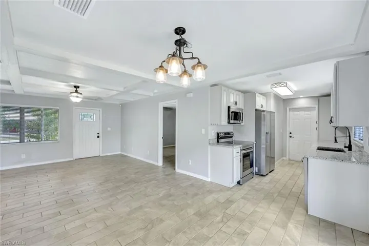 Kitchen featuring stainless steel appliances, a sink, baseboards, a chandelier, and beamed ceiling