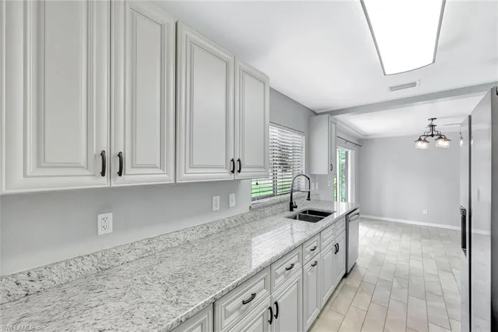 Kitchen with a sink, stainless steel dishwasher, white cabinetry, light stone countertops, and baseboards