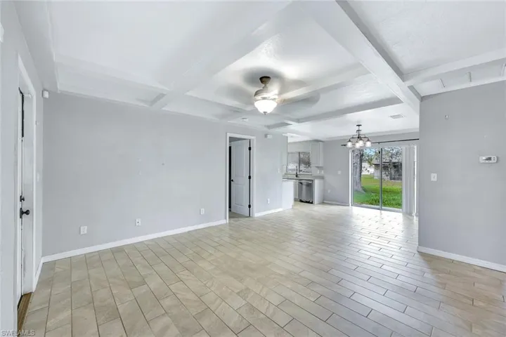 Unfurnished living room with coffered ceiling, a ceiling fan, a chandelier, beamed ceiling, and baseboards