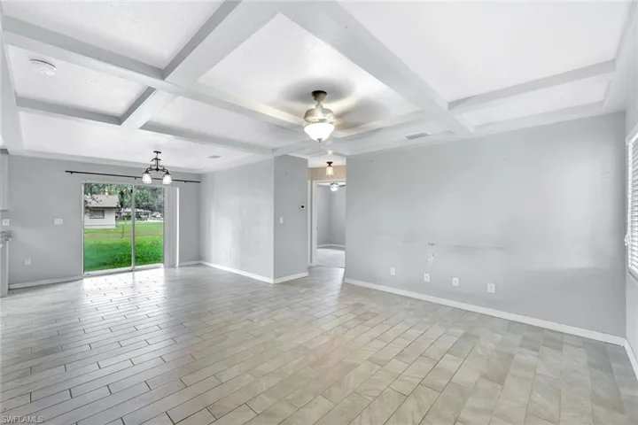 Empty room featuring coffered ceiling, ceiling fan, baseboards, beam ceiling, and a chandelier