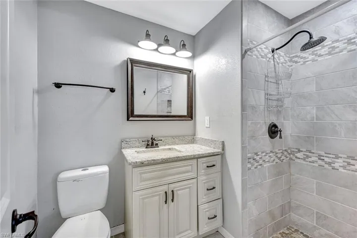 Bathroom with tiled shower, vanity, and toilet