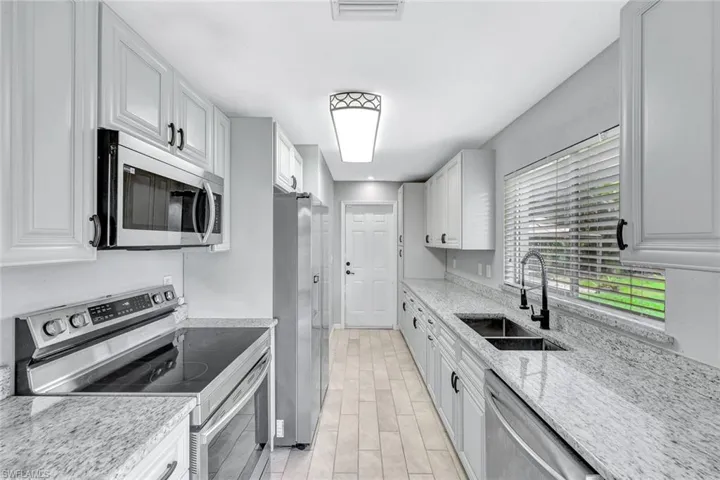 Kitchen featuring appliances with stainless steel finishes, a sink, light stone counters, and white cabinets