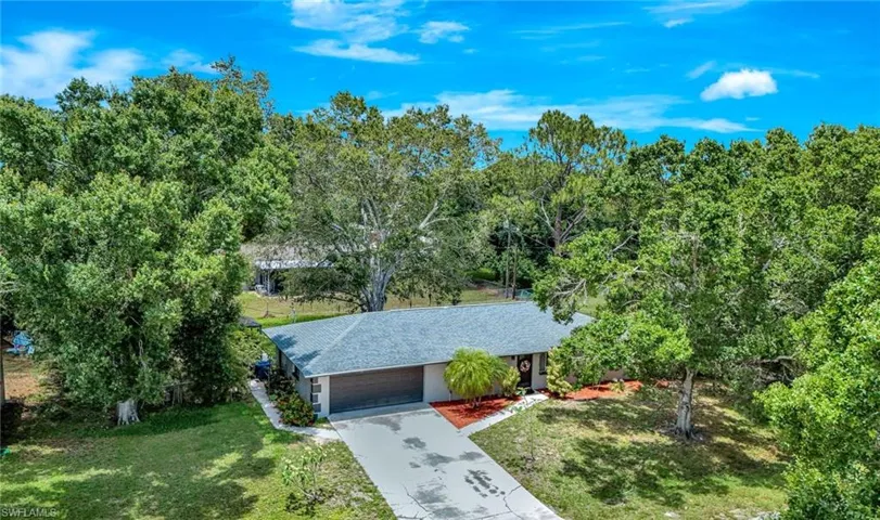 View of property hidden behind natural elements with a front yard, a shingled roof, concrete driveway, a garage, and stucco siding