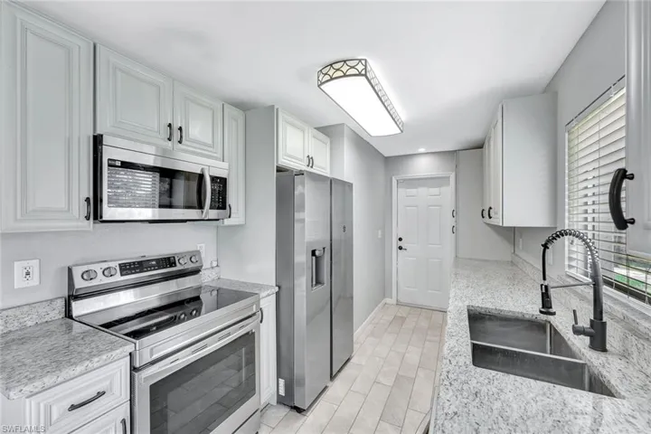 Kitchen with stainless steel appliances, a sink, white cabinetry, baseboards, and light wood-style flooring