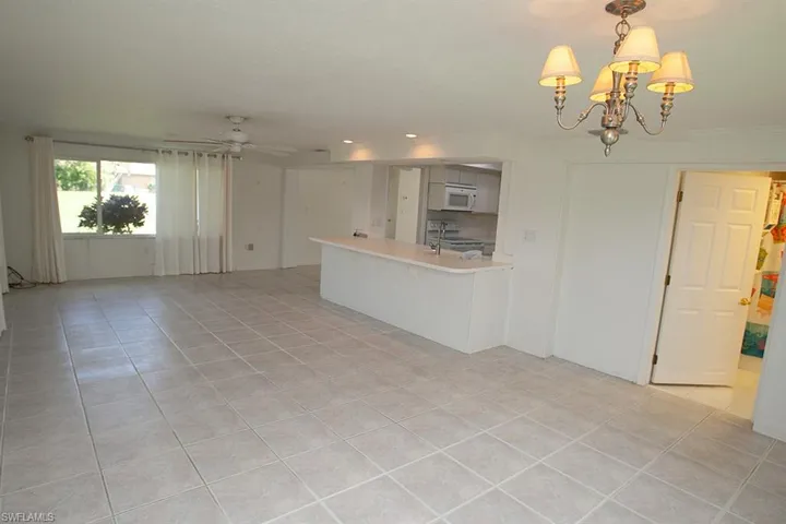 Unfurnished living room featuring light tile patterned floors, sink, and ceiling fan with notable chandelier