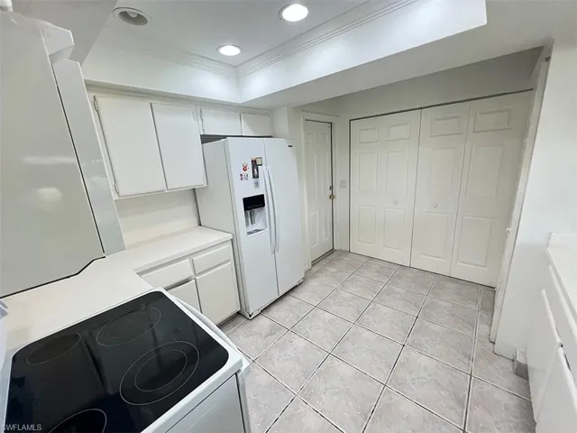 Kitchen with white refrigerator with ice dispenser, crown molding, light tile patterned floors, electric range, and white cabinets