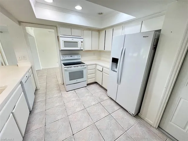 Kitchen with ornamental molding, a raised ceiling, white appliances, and light tile patterned flooring
