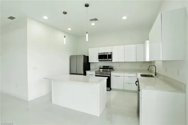 Kitchen with white cabinets, appliances with stainless steel finishes, hanging light fixtures, a kitchen island, and light stone counters