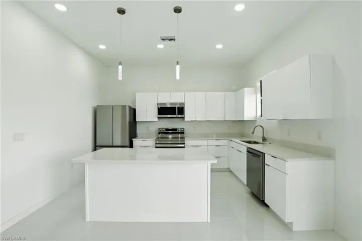 Kitchen featuring white cabinets, stainless steel appliances, a center island, decorative light fixtures, and recessed lighting