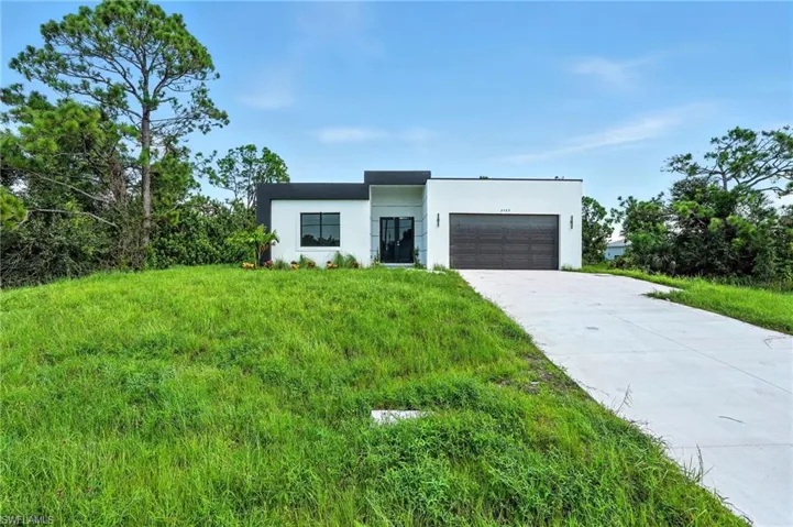 Contemporary house featuring an attached garage, concrete driveway, stucco siding, and a front yard