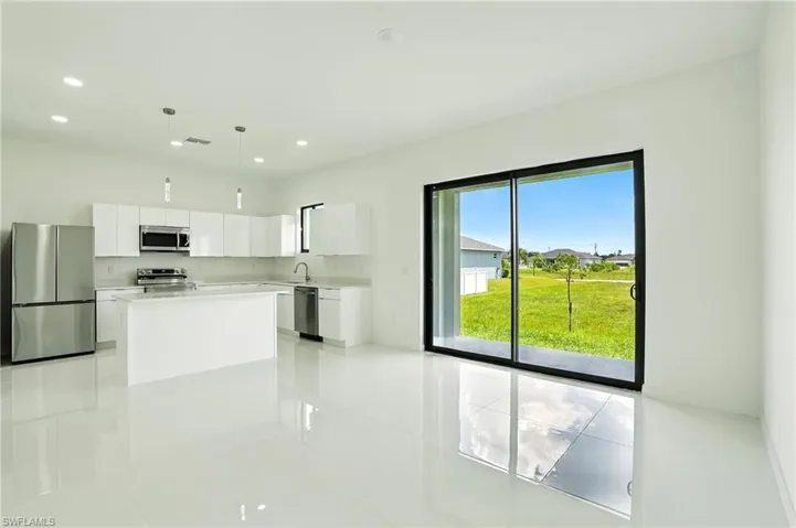 Kitchen featuring appliances with stainless steel finishes, white cabinets, decorative light fixtures, light tile patterned floors, and a kitchen island