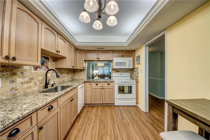 Kitchen with white appliances, light wood-style flooring, hanging lights, light stone counters, and tasteful backsplash
