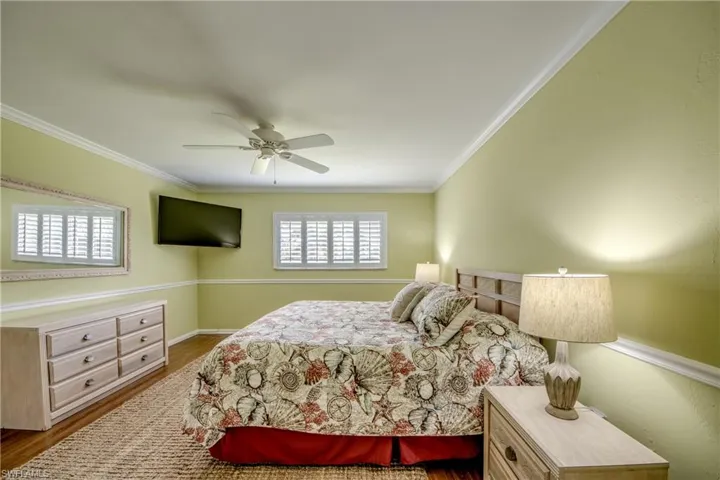 Bedroom with dark wood-type flooring, ornamental molding, and a ceiling fan