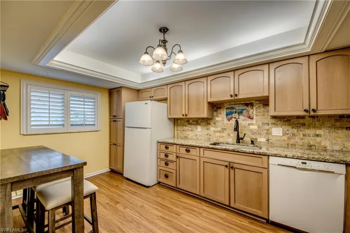 Kitchen featuring white appliances, suspended lighting, light wood finish cabinetry, light stone counters, and light wood-style floors