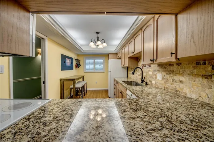 Kitchen with light wood finished floors, light stone countertops, a chandelier, light wood finish cabinets, and a raised ceiling
