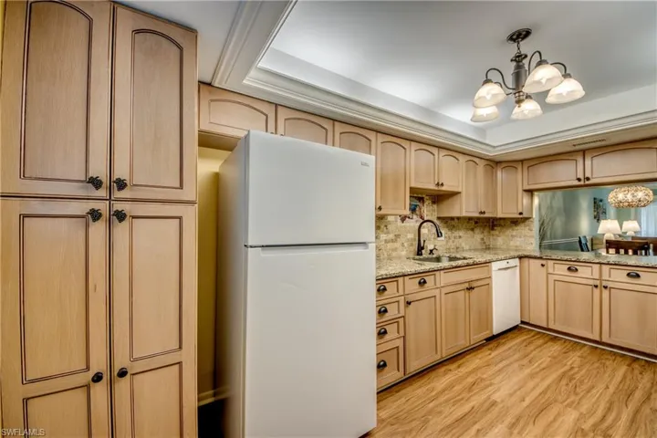 Kitchen featuring a chandelier, light wood finish cabinets, white appliances, and a tray ceiling