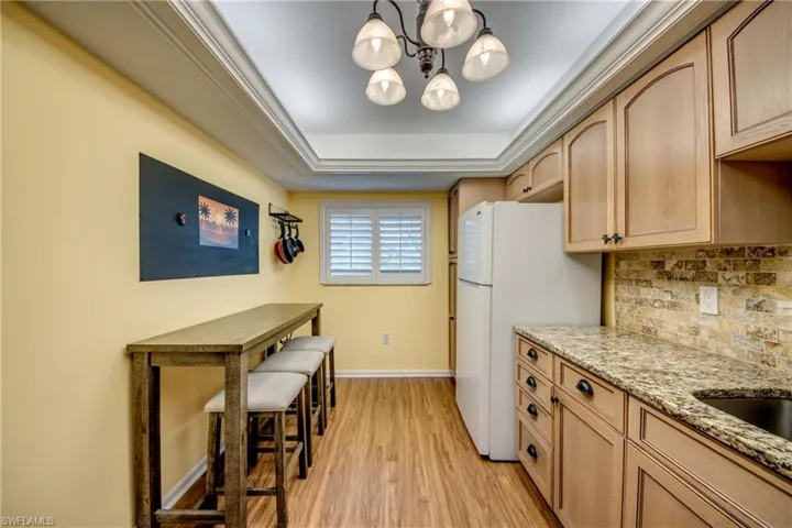 Kitchen featuring light wood-style floors, light stone countertops, hanging lights, freestanding refrigerator, and tasteful backsplash