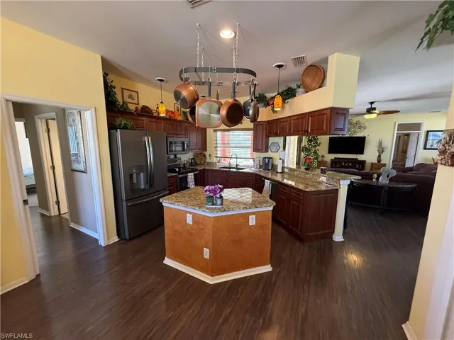 Kitchen with light stone countertops, stainless steel appliances, a kitchen island, a peninsula, and dark wood-type flooring