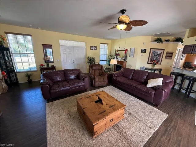 Living area with ceiling fan, healthy amount of natural light, and dark wood-style flooring