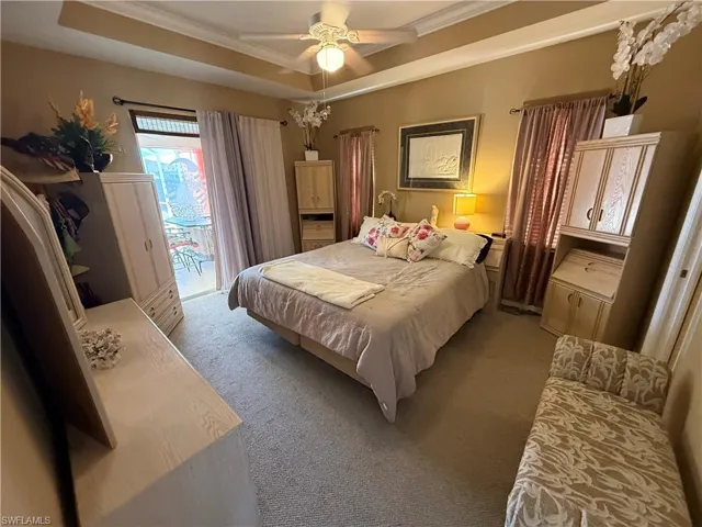 Carpeted bedroom with access to exterior, ornamental molding, a tray ceiling, and a ceiling fan