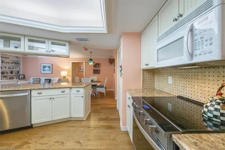 Kitchen with light stone countertops, light wood-style floors, appliances with stainless steel finishes, decorative light fixtures, and tasteful backsplash