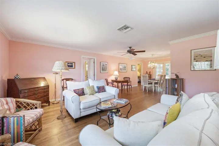 Living area featuring visible vents, ceiling fan with notable chandelier, light wood-style floors, and ornamental molding