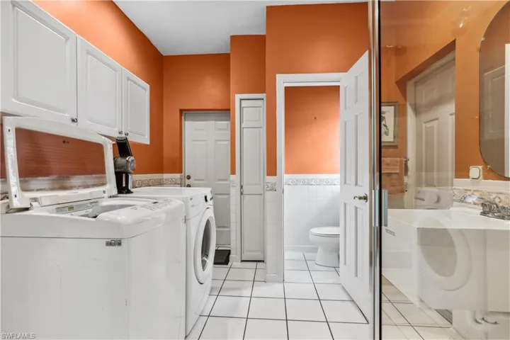 Laundry room with tile walls, extra cabinets, washer, dryer, laundry tub and full bath