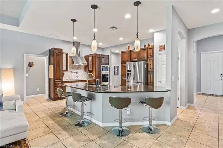 Kitchen featuring a kitchen breakfast bar, hanging light fixtures, a large island with sink, stainless steel appliances, and wall chimney exhaust hood