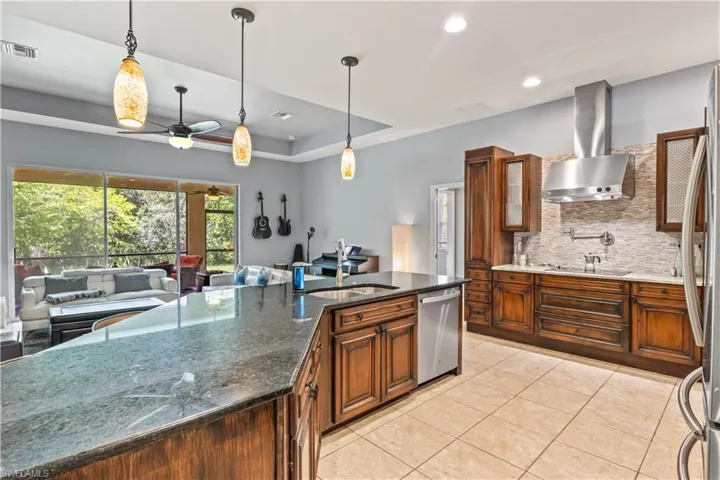 Kitchen featuring sink, stainless steel dishwasher, pendant lighting, dark stone counters, and wall chimney range hood