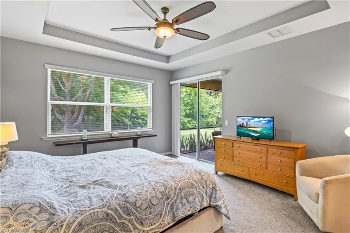 Carpeted bedroom featuring access to outside, ceiling fan, and a tray ceiling