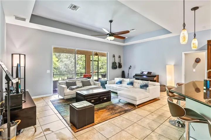 Living room featuring light tile patterned floors, a tray ceiling, and ceiling fan