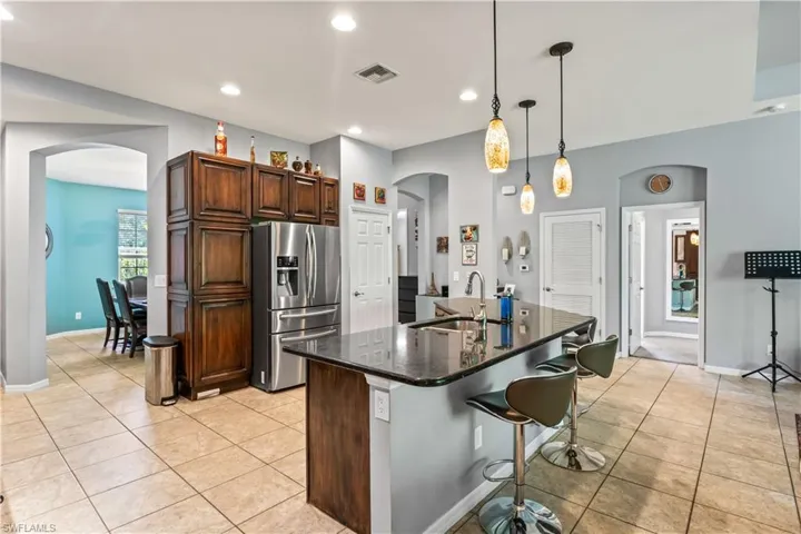 Kitchen with decorative light fixtures, an island with sink, sink, stainless steel fridge, and light tile patterned floors