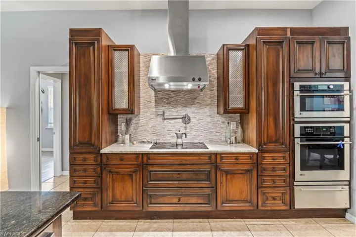 Kitchen with stone countertops, ventilation hood, light tile patterned floors, black electric cooktop, and backsplash