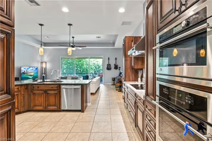 Kitchen featuring appliances with stainless steel finishes, sink, light tile patterned floors, ceiling fan, and a raised ceiling