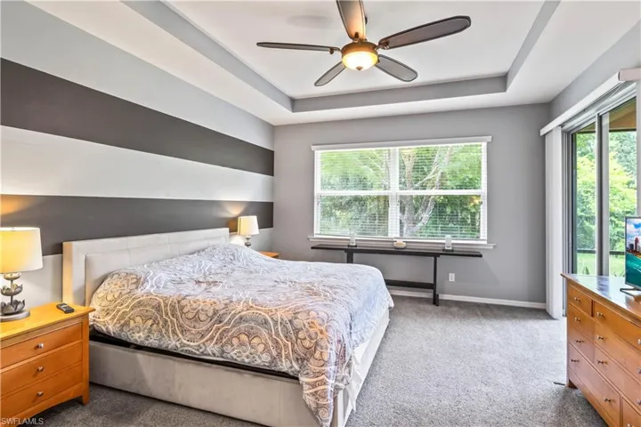 Carpeted bedroom featuring a raised ceiling and ceiling fan