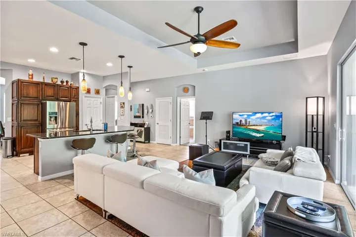 Living room featuring ceiling fan, a tray ceiling, sink, and light tile patterned floors