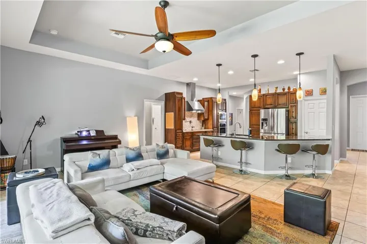 Tiled living room featuring ceiling fan, a tray ceiling, and sink