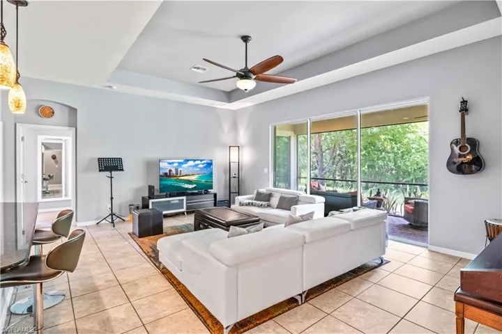 Living room featuring a raised ceiling, light tile patterned flooring, and ceiling fan