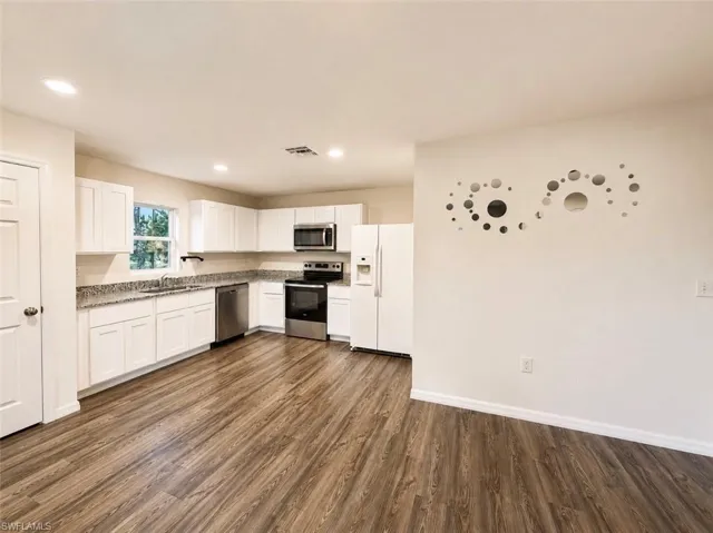 Open-concept kitchen featuring white cabinetry, granite countertops, stainless steel appliances, wood-finish flooring, and recessed lighting