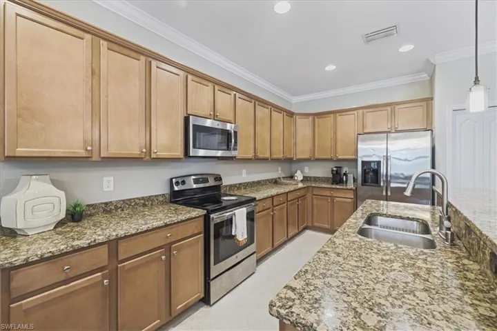 Kitchen with appliances with stainless steel finishes, ornamental molding, stone counters, brown cabinetry, and decorative light fixtures