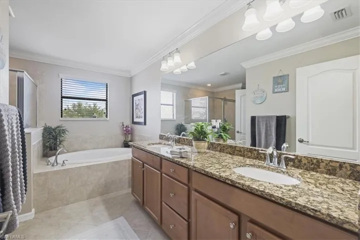 Bathroom with double vanity, a stall shower, tile patterned floors, a garden tub, and crown molding