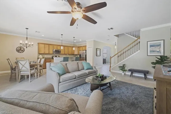 Living area featuring light tile patterned flooring, stairs, ceiling fan, arched walkways, and ornamental molding