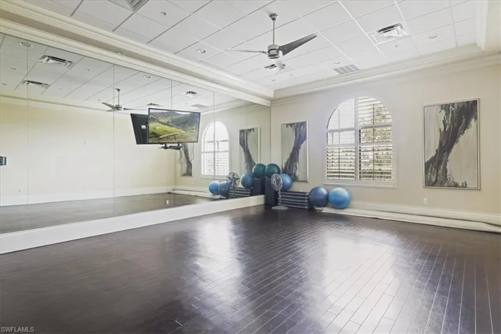 Workout room featuring a drop ceiling, healthy amount of natural light, wood-type flooring, ornamental molding, and ceiling fan
