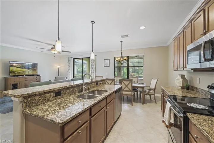 Kitchen with appliances with stainless steel finishes, crown molding, a chandelier, decorative light fixtures, and an island with sink