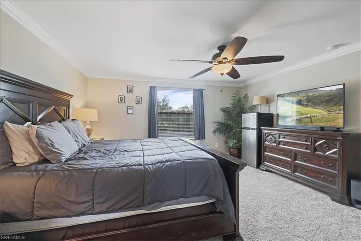 Bedroom with crown molding, carpet flooring, freestanding refrigerator, and a ceiling fan