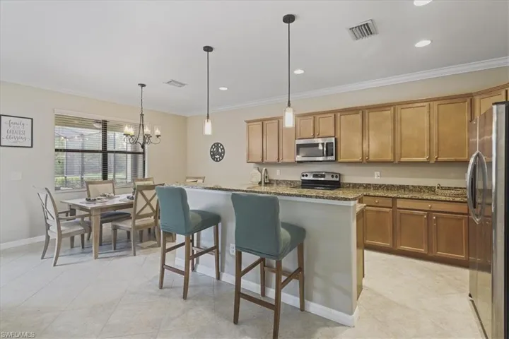 Kitchen featuring appliances with stainless steel finishes, crown molding, brown cabinets, dark stone counters, and a center island with sink