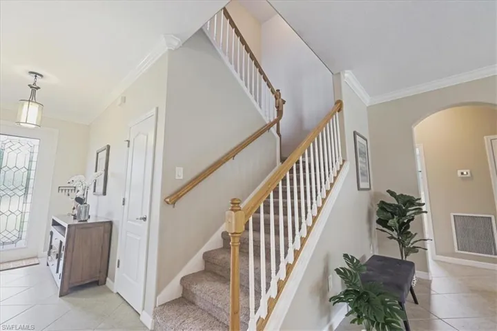 Entryway featuring arched walkways, light tile patterned floors, crown molding, and stairs