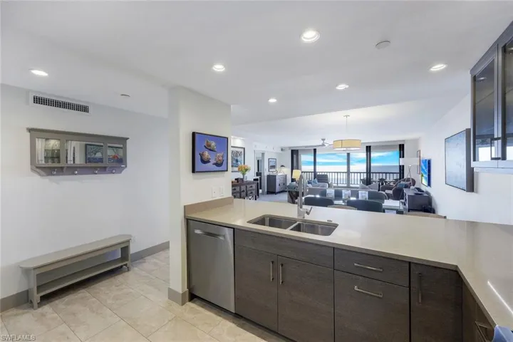 Kitchen with stainless steel dishwasher, dark brown cabinetry, sink, light tile patterned floors, and pendant lighting