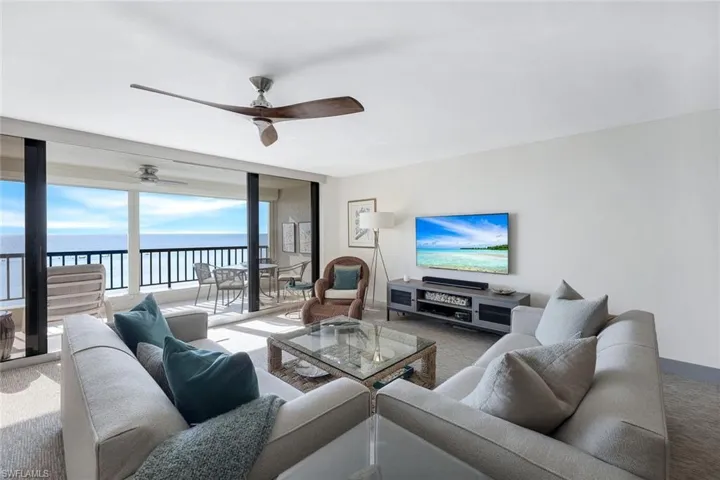 Carpeted living room with a wall of windows, a water view, and ceiling fan